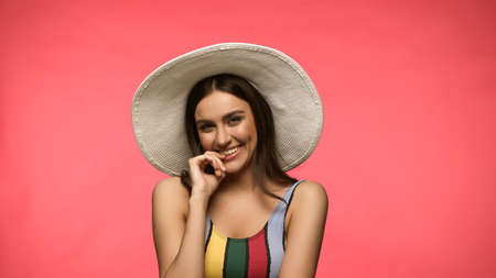 Cheerful woman in swimsuit and sun hat looking at camera isolated on pink