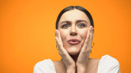 Amazed woman in blouse touching face isolated on orangeの写真素材