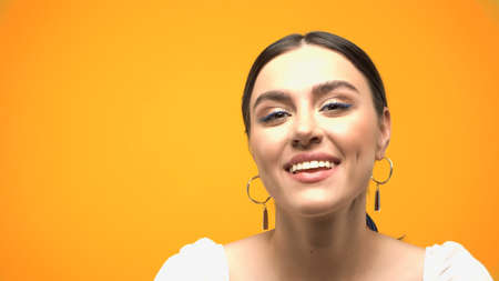 Positive woman in earrings and blouse looking at camera isolated on yellow