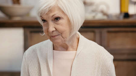 senior woman with grey hair looking away in blurred kitchen
