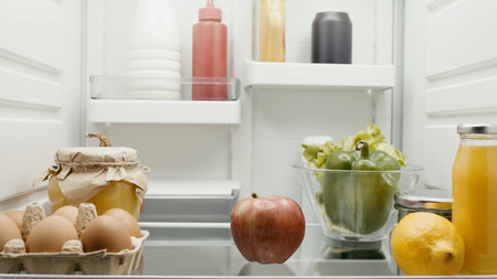 fresh fruits and vegetables near eggs, orange juice and bottles with sauces in fridgeの写真素材