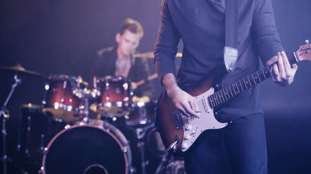 KYIV, UKRAINE - DECEMBER 30, 2021: rock guitarist playing near blurred drummer on stageの写真素材