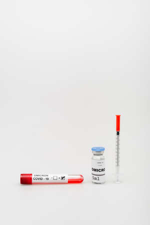 test tube with positive result near covid-19 omicron variant vaccine and syringe on grey background
