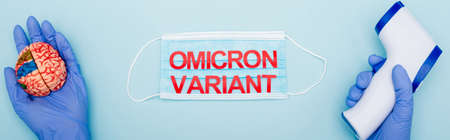 partial view of doctor with brain model and pyrometer near medical mask with omicron variant lettering on blue, bannerの写真素材