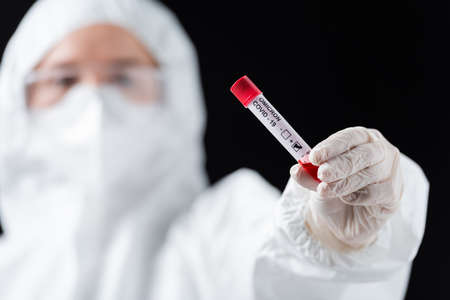 blurred scientist in white hazmat suit holding positive covid-19 omicron variant test isolated on...