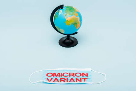 medical mask with red omicron variant lettering near globe on blue background