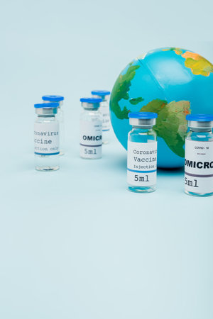 covid-19 and omicron strain vaccine jars near globe on blueの写真素材