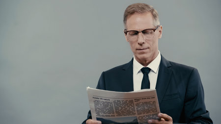 Businessman in eyeglasses reading newspaper isolated on grey