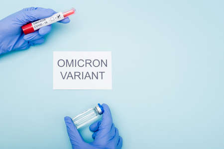 top view of doctor in latex gloves holding test tube and vaccine vial near card with omicron variant lettering on blueの写真素材