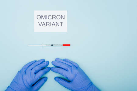 top view of doctor in latex gloves near card with omicron variant lettering and syringe on blueの写真素材
