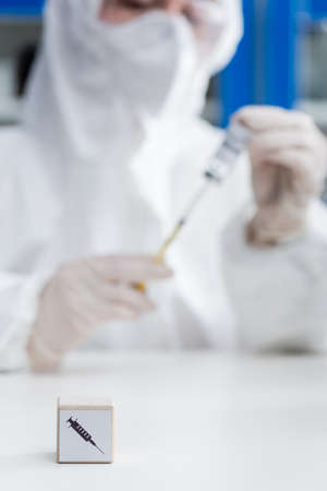cropped view of blurred immunologist in hazmat suit holding vaccine near cube with syringe icon, variant conceptの写真素材