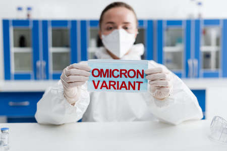 blurred scientist in hazmat suit holding protective mask with variant letteringの写真素材