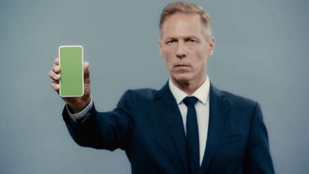 Smartphone with green screen in hand of blurred businessman isolated on grey