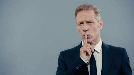 Mature businessman showing secret gesture isolated on greyの写真素材