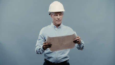 Smiling engineer in hardhat looking at blueprint isolated on grey