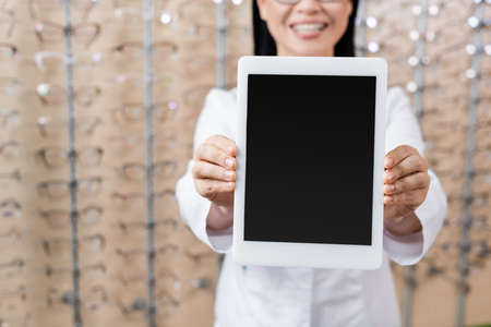 cropped view of blurred oculist showing digital tablet with blank screen in optics store