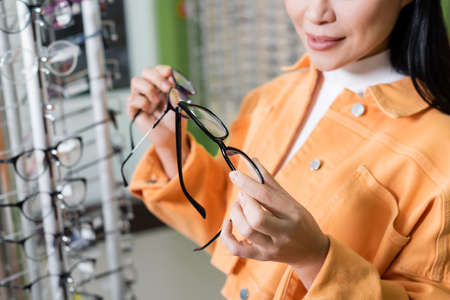 cropped view of blurred woman comparing eyeglasses in optics shopの写真素材