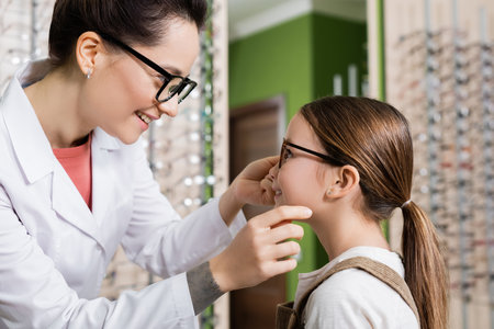 side view of smiling ophthalmologist trying eyeglasses on child in optics salonの写真素材