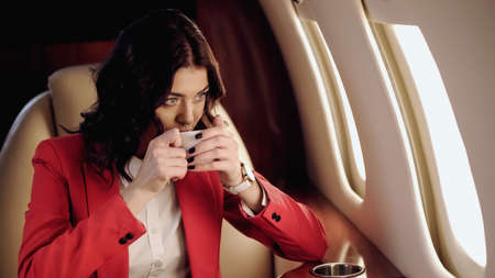 Businesswoman drinking coffee and looking at window in private plane