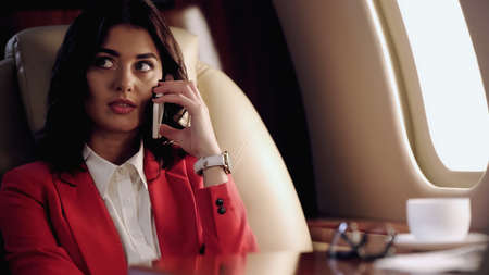 Businesswoman talking on cellphone near blurred cup in private plane