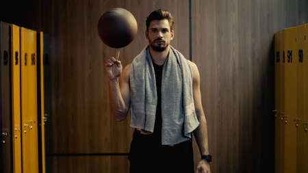 young sportsman spinning basketball in finger in locker room