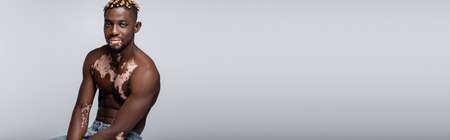 young african american man with vitiligo and trendy hairstyle sitting on grey, bannerの写真素材