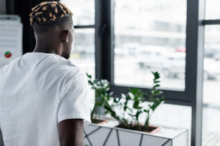 back view of african american man with trendy hairstyle listening music in earphone in officeの写真素材