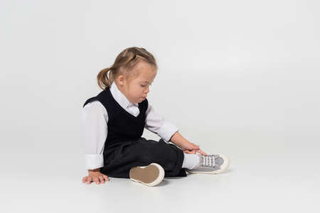full length of kid with down syndrome in vest and white shirt sitting on greyの写真素材