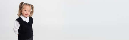 happy kid with down syndrome in vest and white shirt standing isolated on grey, bannerの写真素材