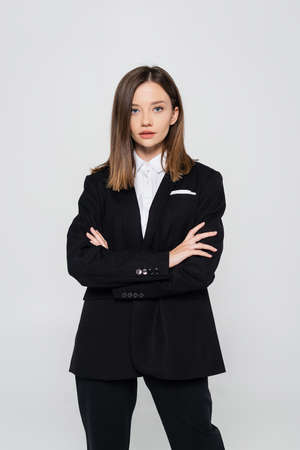 stylish woman in suit standing with crossed arms isolated on greyの写真素材