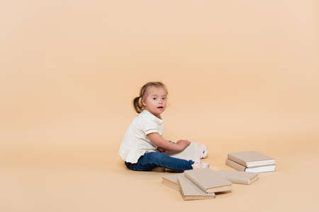 girl with down syndrome sitting near books on beigeの写真素材