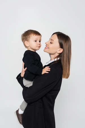 happy mother holding in arms toddler son isolated on greyの写真素材