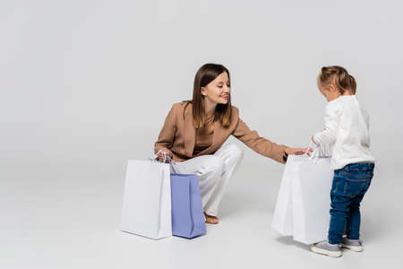 happy and stylish mother holding shopping bags near girl with down syndrome on greyの写真素材