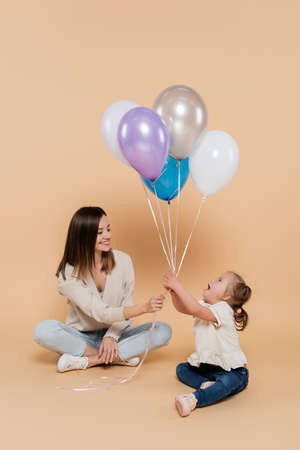 positive woman giving colorful balloons to girl with down syndrome on beigeの写真素材