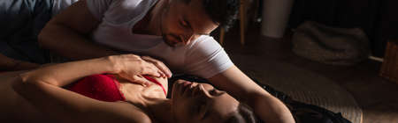 young man in white t-shirt near sexy woman with closed eyes in dark bedroom, banner