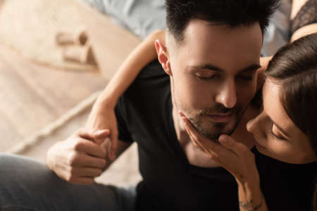 overhead view of sensual woman touching face of man holding her hand in bedroom