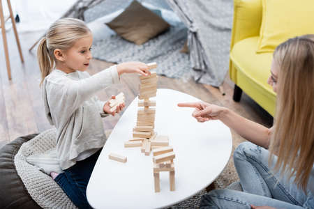 Blurred woman pointing at wood blocks game while child playing near coffee tableの写真素材