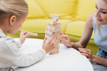 Blurred child playing wood blocks game with parent on coffee table at homeの写真素材