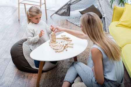 Parent and kid playing wood blocks game on coffee table near couch at homeの写真素材