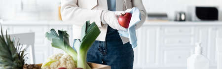 Cropped view of woman in latex gloves cleaning apple with rag near fresh food at home, bannerの写真素材