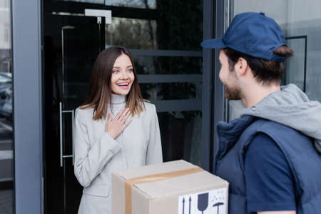 Excited woman looking at blurred courier near door of building outdoorsの写真素材