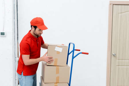Courier in uniform taking carton box on cart in hallwayの写真素材