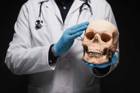 cropped view of blurred physician in latex gloves holding skull isolated on blackの写真素材