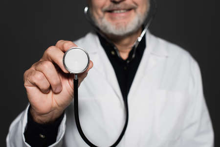 cropped view of blurred smiling physician holding stethoscope isolated on blackの写真素材