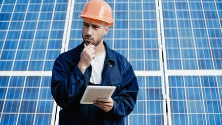 thoughtful engineer using digital tablet near solar panel