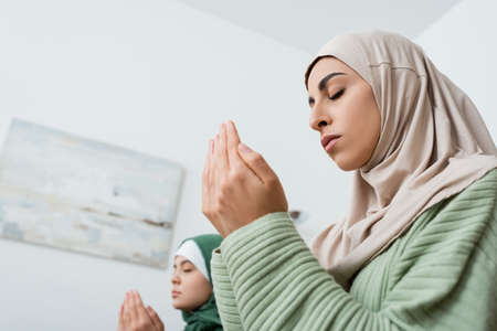 Low angle view of arabian woman praying near blurred daughter at homeの写真素材