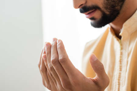 Cropped view of hands of blurred arabian man praying at home
