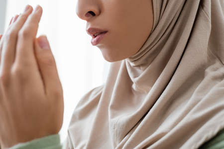 Cropped view of young arabian woman in traditional hijab praying at home