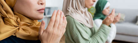 Arabian woman praying near blurred family at home, bannerの写真素材