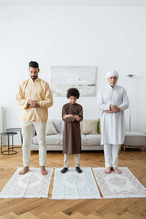 Multiethnic men and arabian boy praying on rugs at homeの写真素材